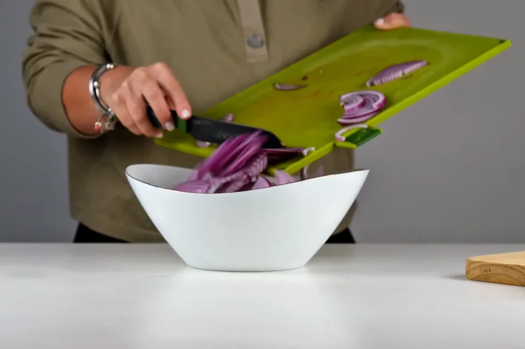 La cebolla morada en juliana pasa de la tabla al bowl con el pescado
