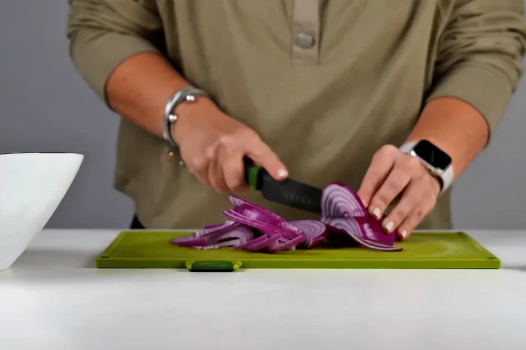 Cebolla morada cortada en juliana con cuchillo sobre una tabla verde