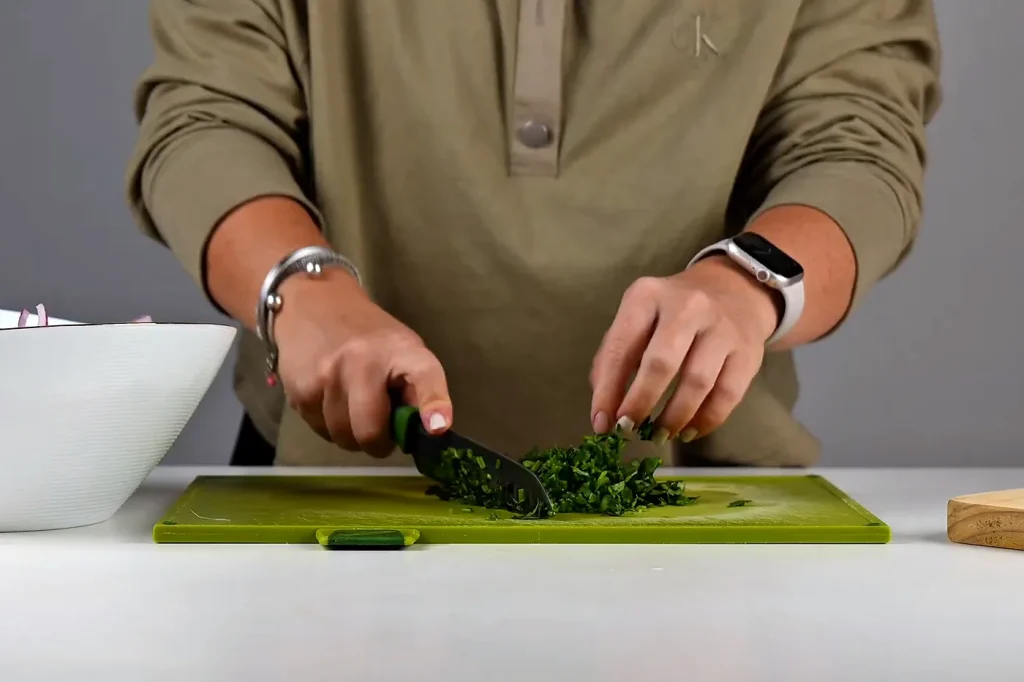 Culantro picado finamente con cuchillo sobre una tabla verde