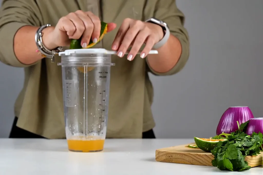 Manos exprimiendo un limón sobre un colador, encima de una taza medidora con jugo