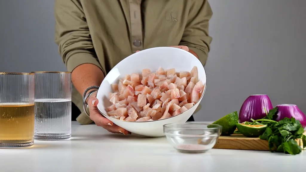 Ingredientes del ceviche: tilapia en cubos en un bowl, ginger ale y soda en vasos, sal, limones, cebolla morada y culantro
