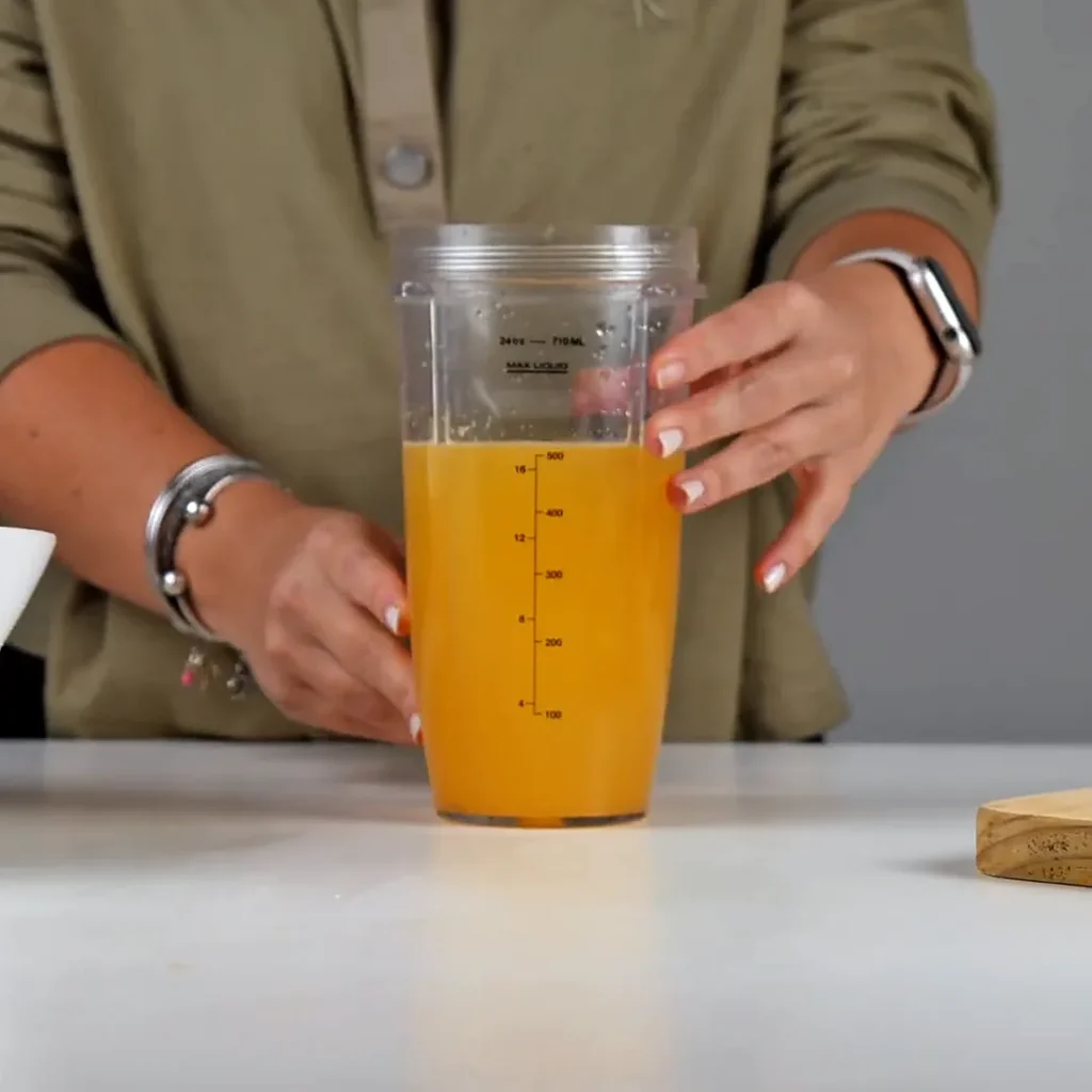Taza medidora llena de jugo de limón mandarina, de color anaranjado