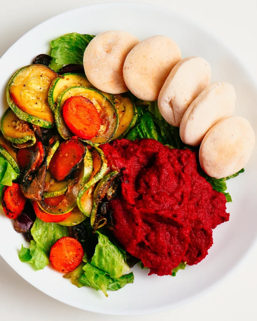 Plato con hummus de remolacha, rodajas de zucchini y zanahoria salteadas, lechuga y cinco panes pita