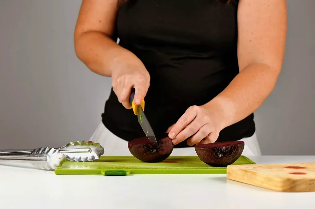 Manos cortando la remolacha cocida en trozos sobre una tabla verde