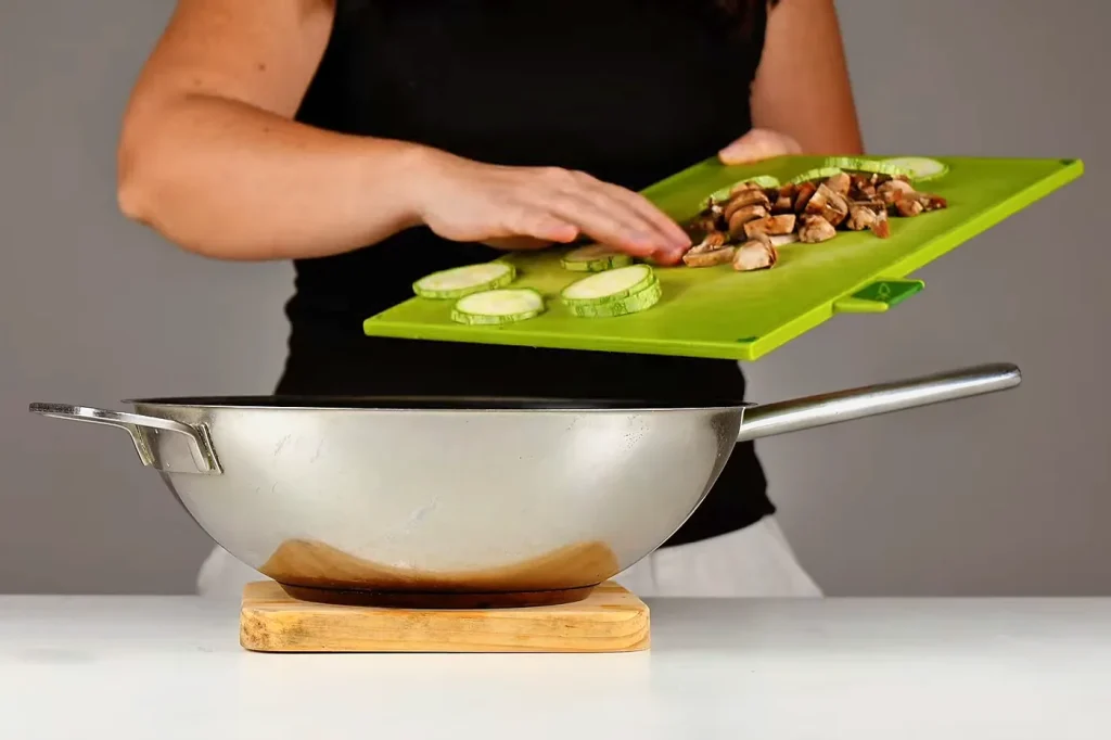 Rodajas de zucchini y hongos en láminas pasando de la tabla al sartén para saltearlos