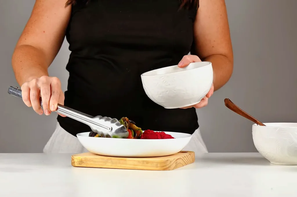 Con unas pinzas se ponen los vegetales salteados junto al hummus de remolacha en el plato