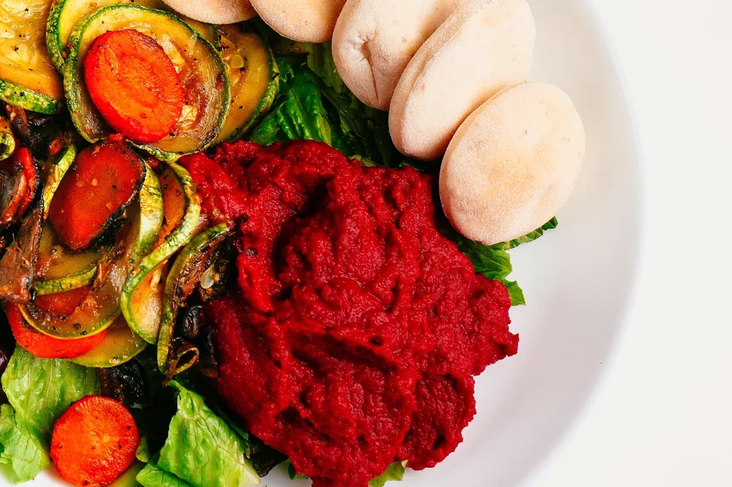Primer plano del hummus de remolacha cremoso junto a los panes pita y el zucchini salteado