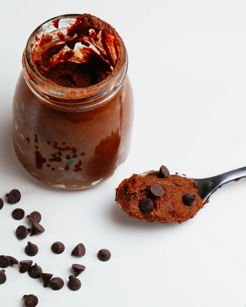 Frasco de vidrio con mousse de chocolate cremoso, una cucharada servida al lado y chispas de chocolate regadas