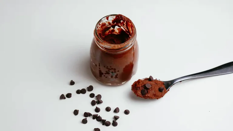 Mousse de chocolate en un frasco de vidrio, con una cuchara llena de mousse y chispas de chocolate sobre una mesa blanca