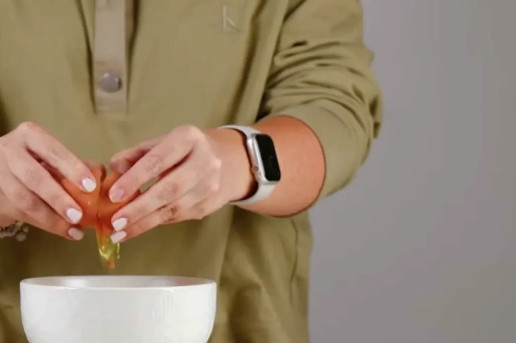 Manos quebrando un huevo sobre un bowl blanco para preparar el mousse de chocolate